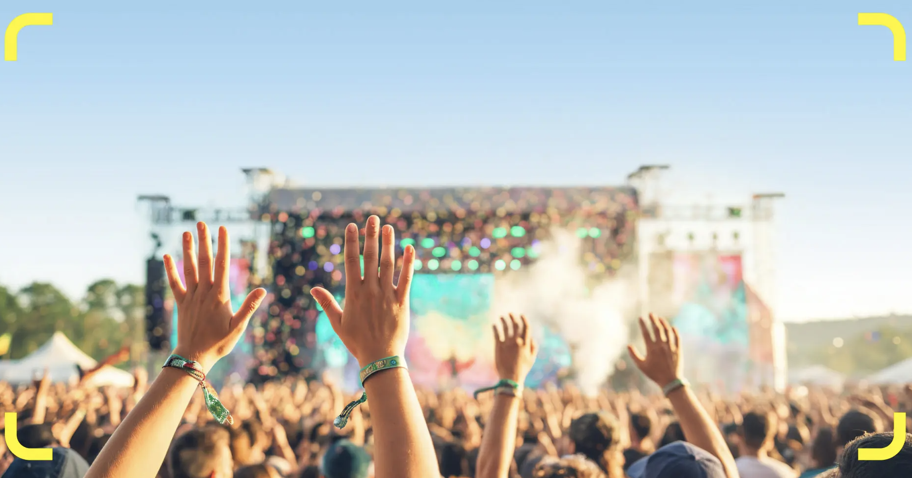Festival crowd with raised hands and wristbands facing the main stage